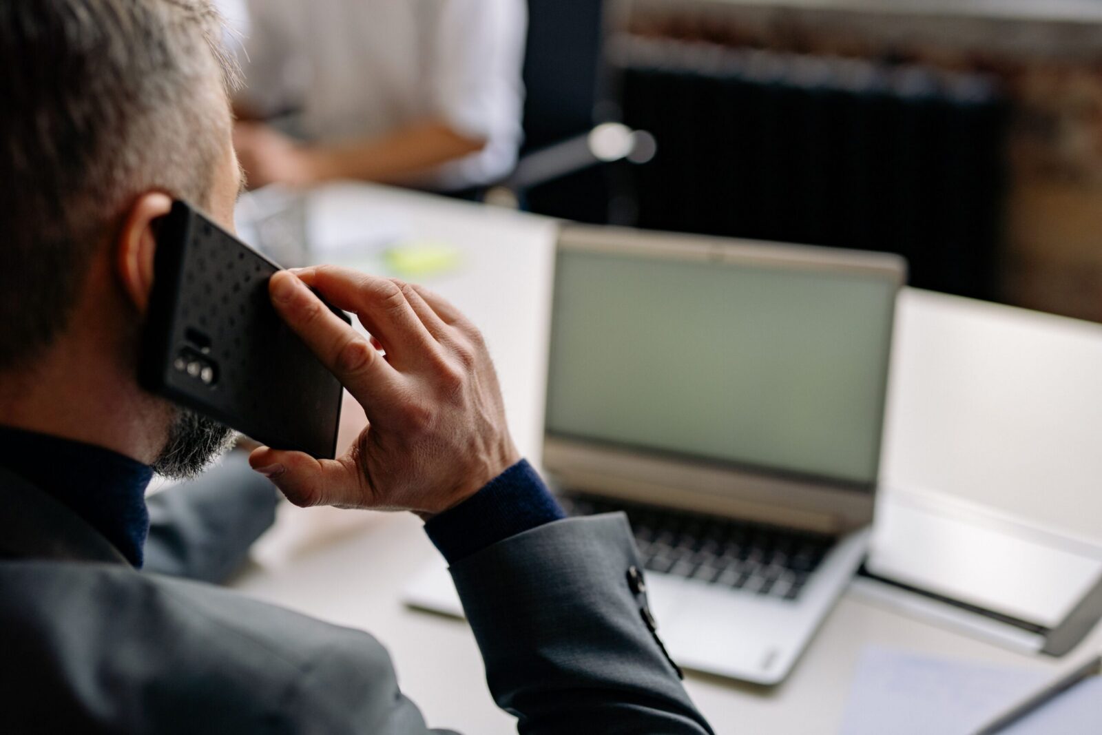 Professional man using cellphone in office setting, multitasking with a laptop.